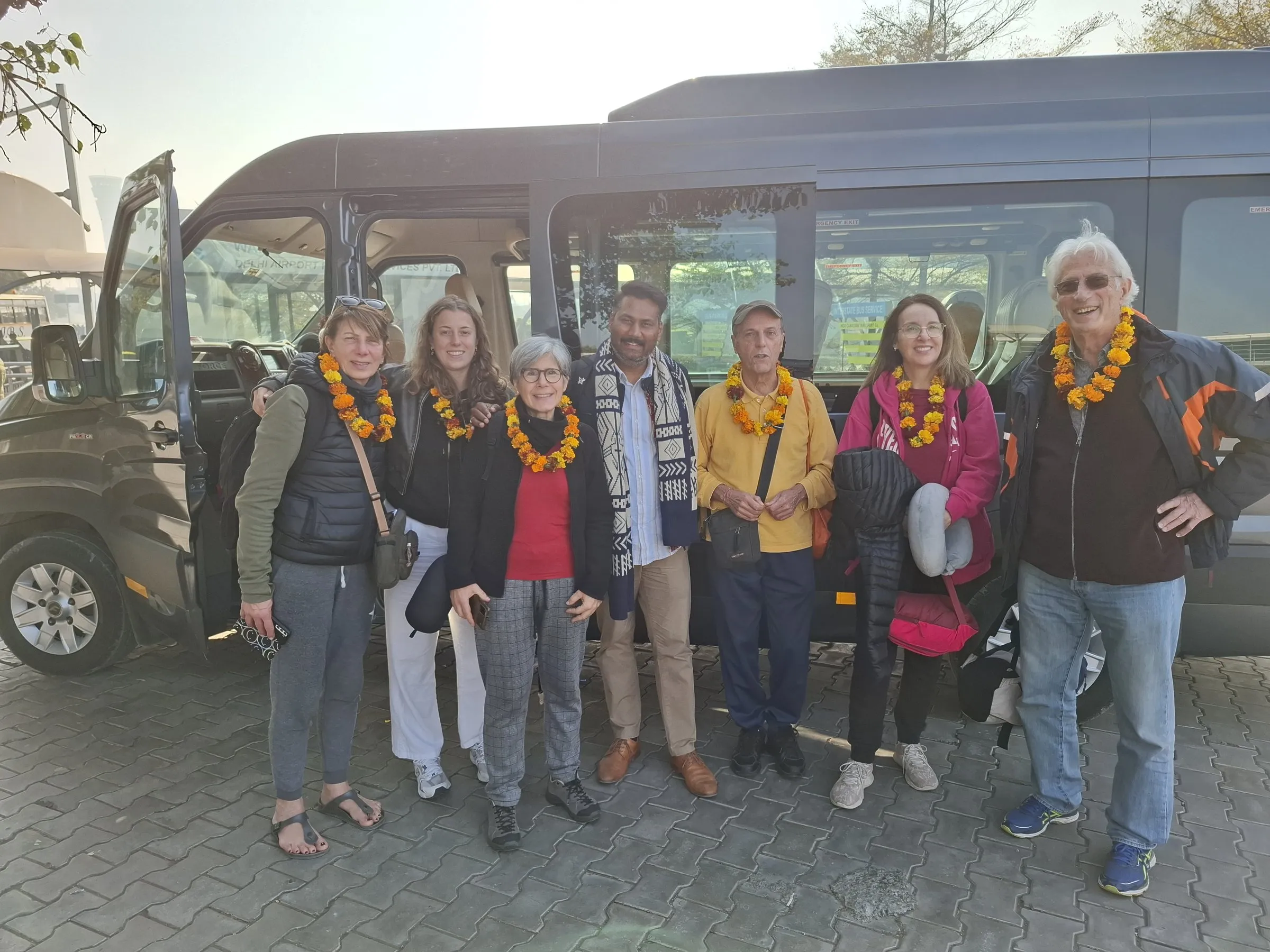 Travellers in marigold garlands beside their coach, on arrival