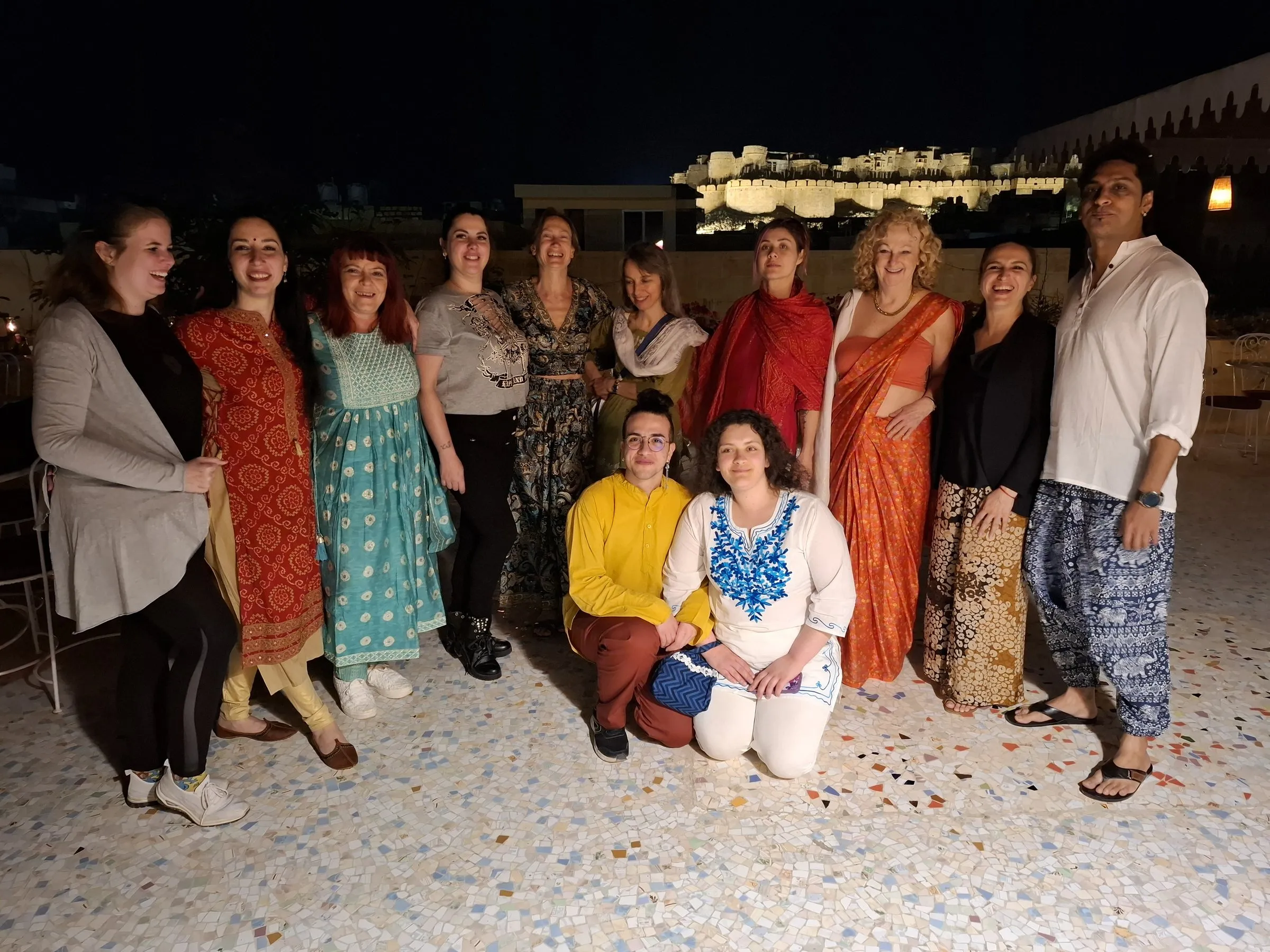 Travellers on a rooftop at night, the fort lit behind them