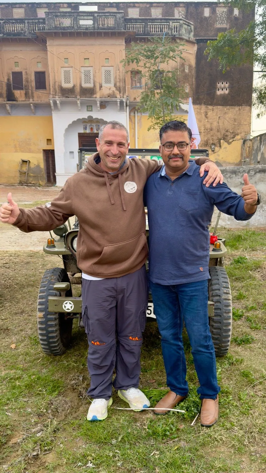 Two men by a jeep in front of an old painted haveli