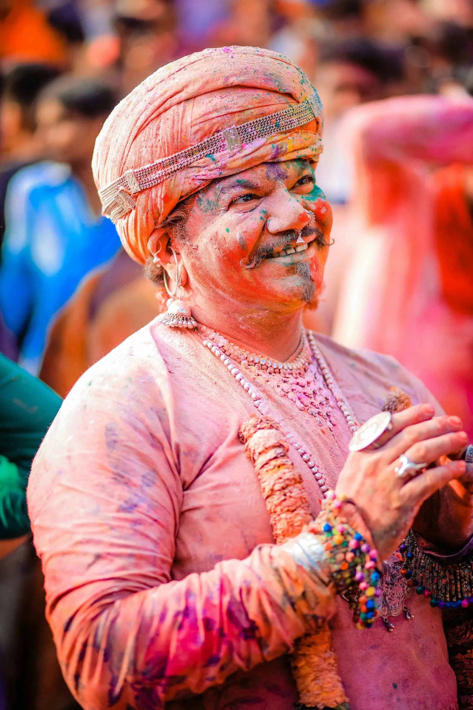 A man in a pink turban covered in Holi colour, laughing, in Vrindavan