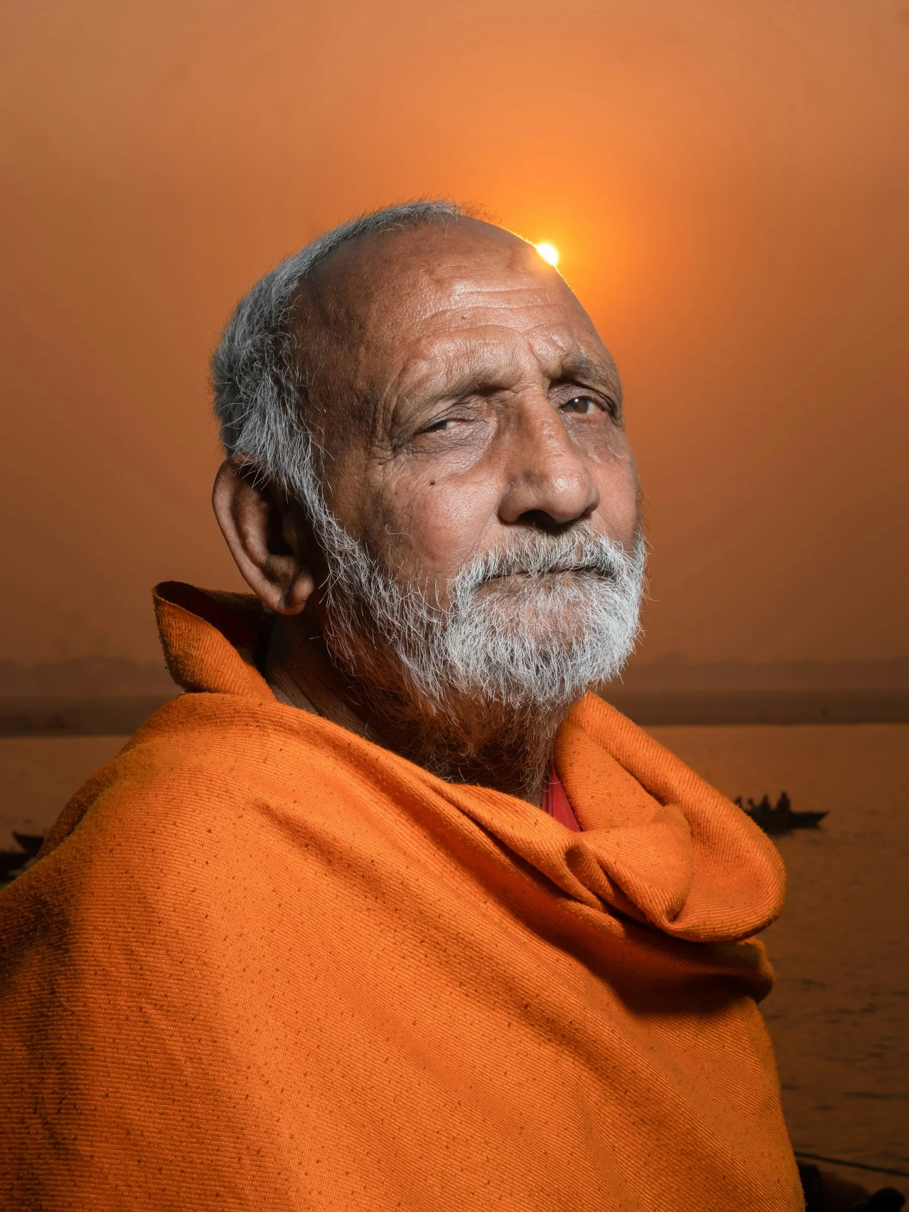 An elder in a saffron shawl at dawn beside the Ganga in Varanasi