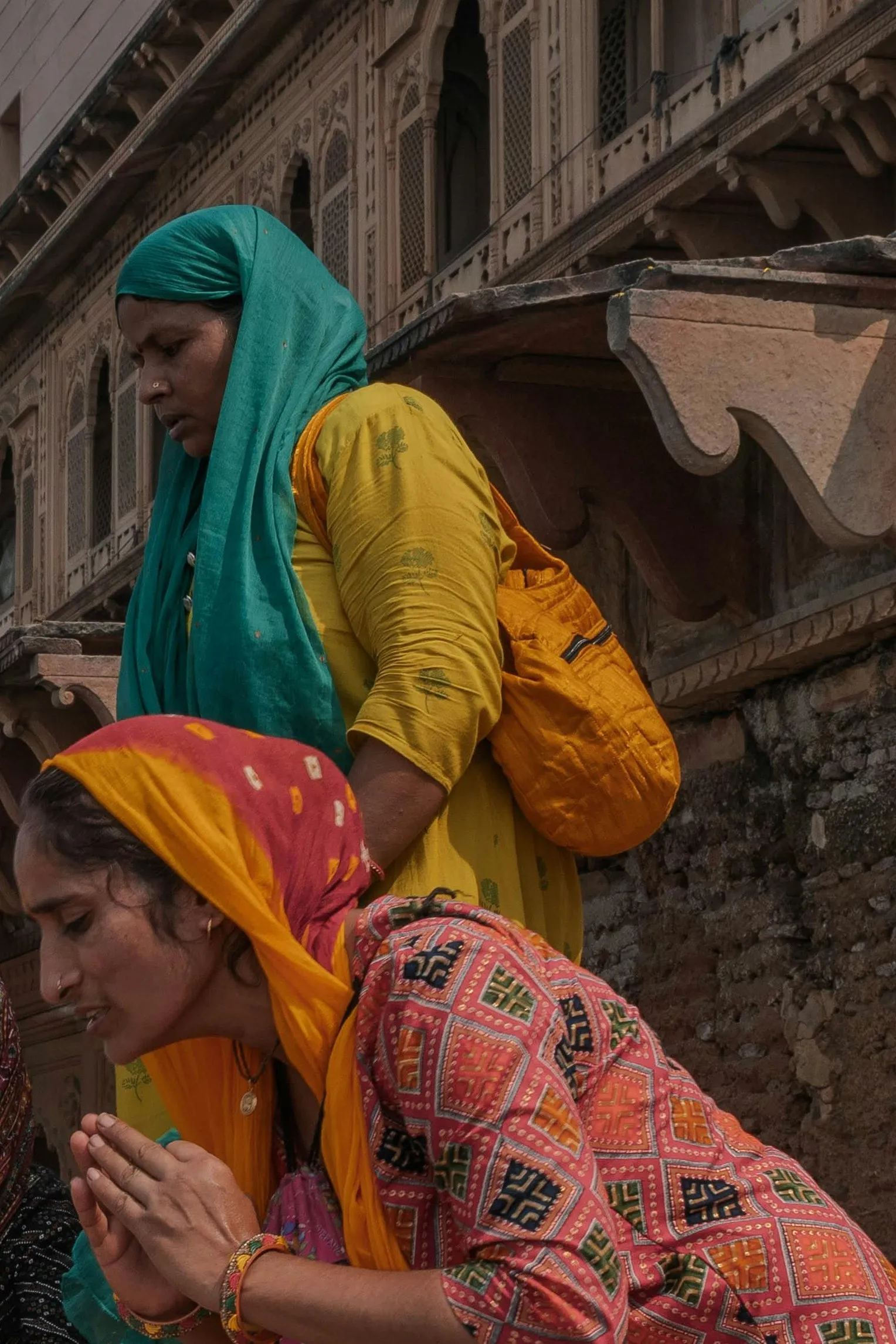 Two women at prayer on the ghat at Maheshwar, one in a teal veil, one in orange