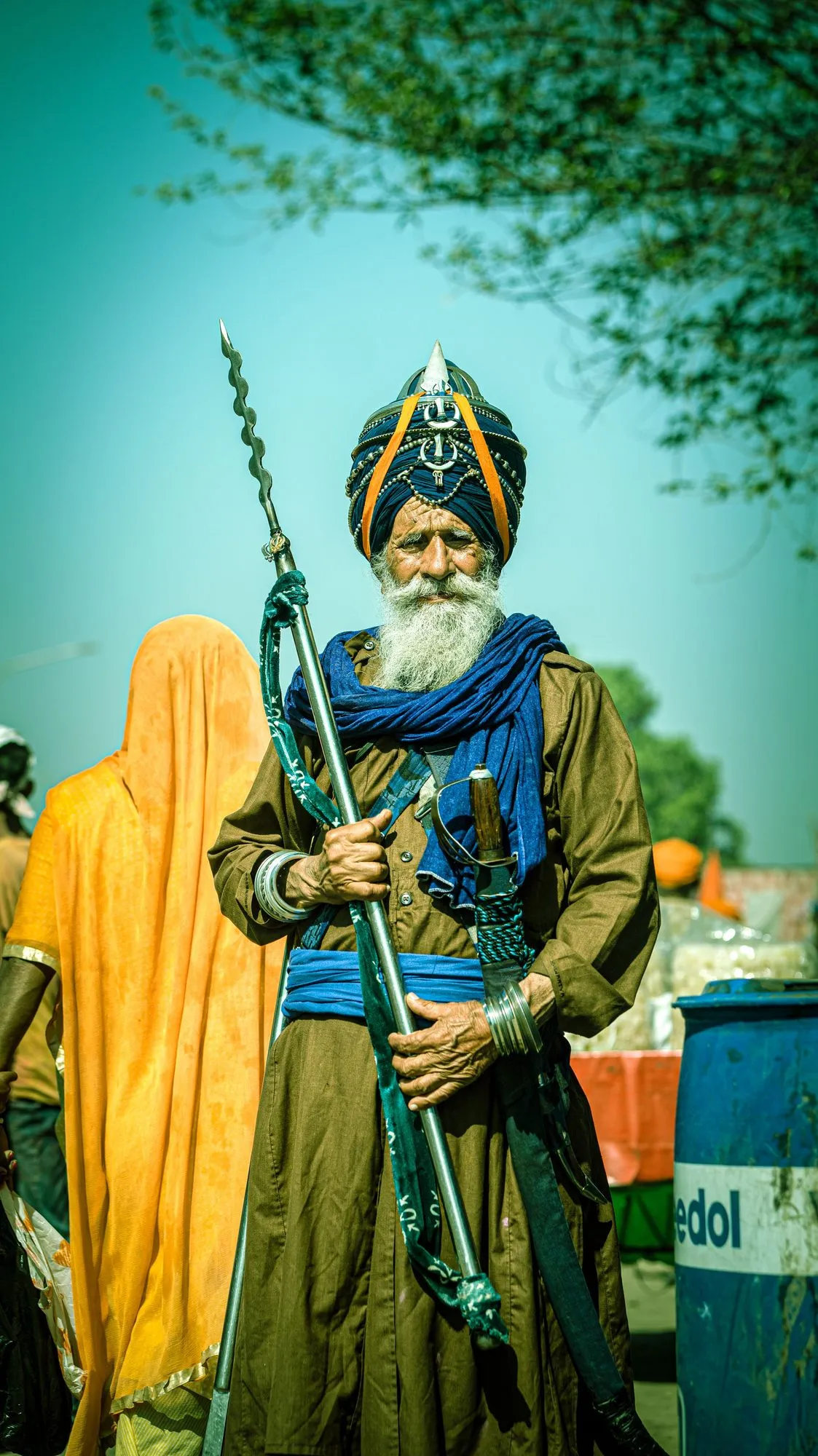 A Nihang Sikh elder in blue robes and turban, holding his spear