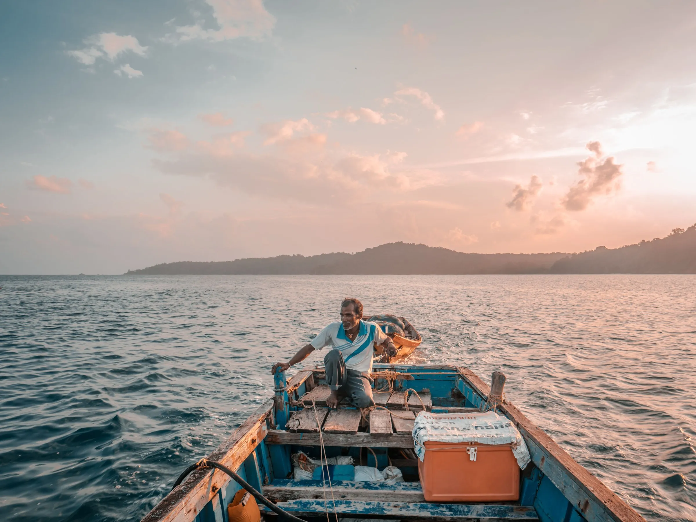 A fisherman at the tiller of his wooden boat at sunrise on the Andaman Sea