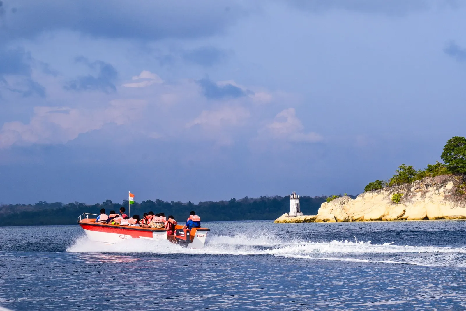 A speedboat full of passengers passing a small lighthouse on the Andaman coast
