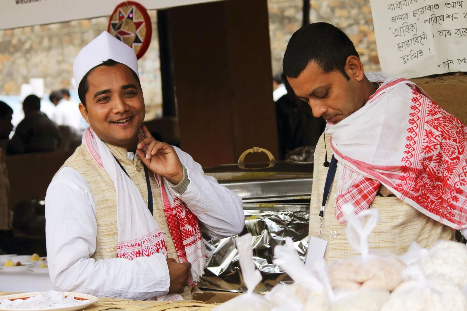 Two Assamese men in red-and-white gamosas at a market stall in Assam