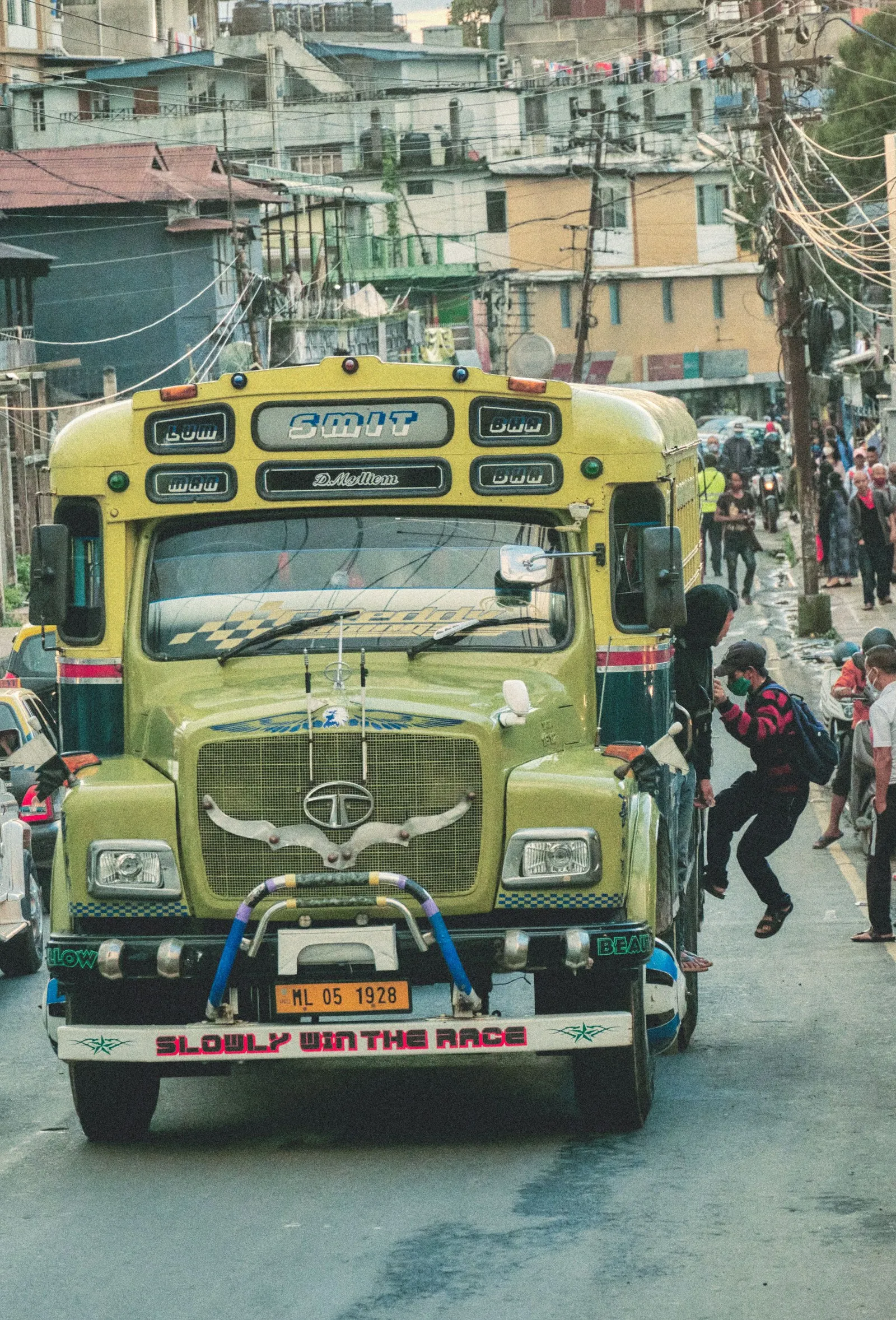 Passengers hopping on to a painted Tata bus on a hill street in Shillong