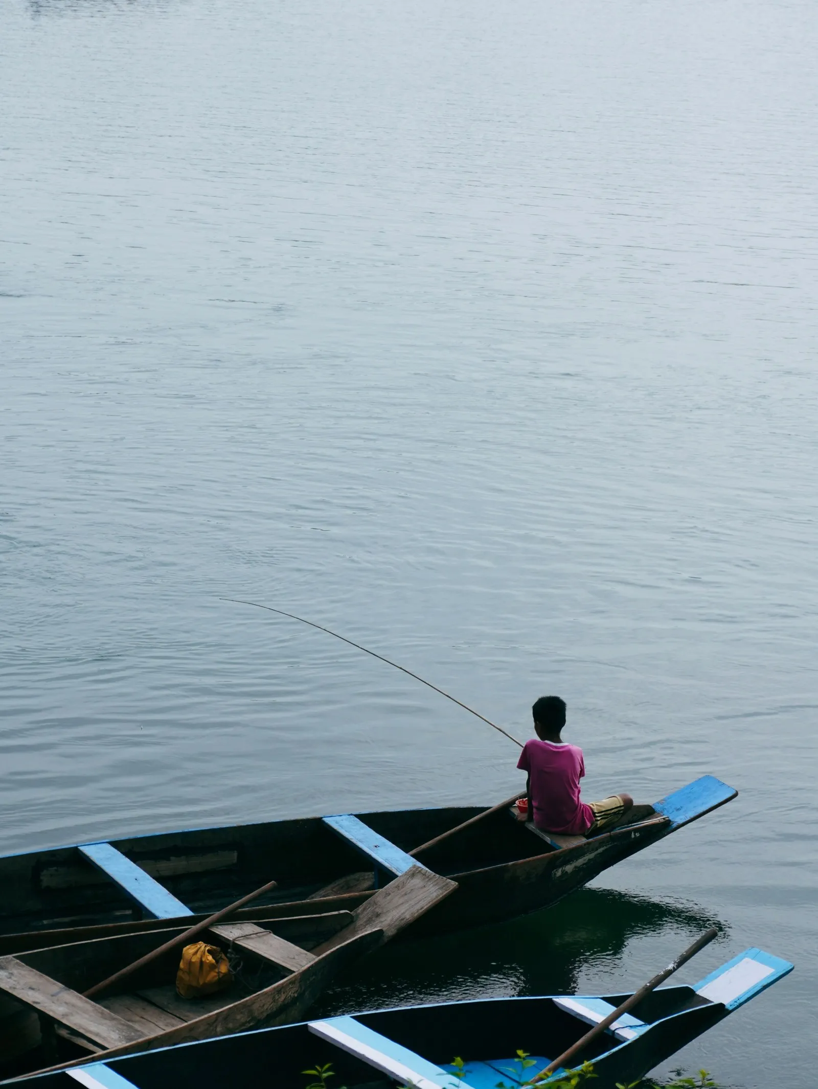 A fisherman casting from a wooden boat on the Umngot, the Dawki river