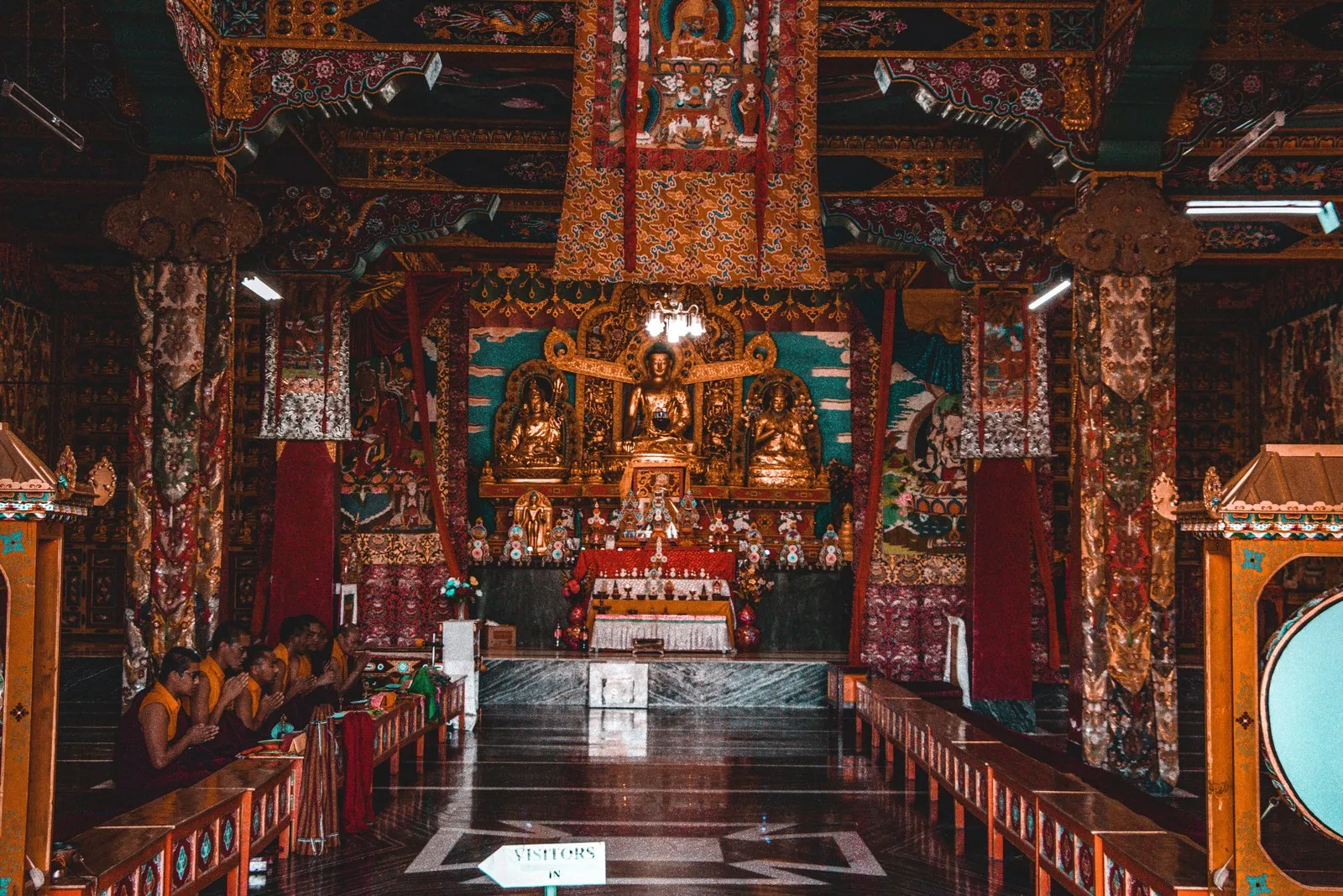 Monks at prayer below the golden images of a monastery hall in Sikkim