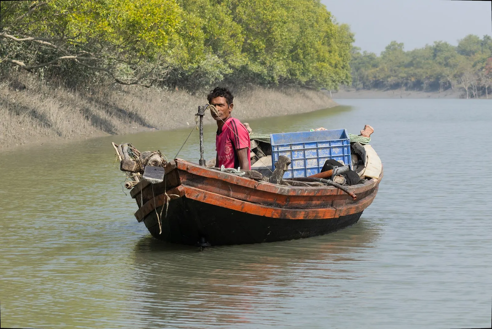 A fisherman in his wooden boat on a creek of the Sundarbans, West Bengal