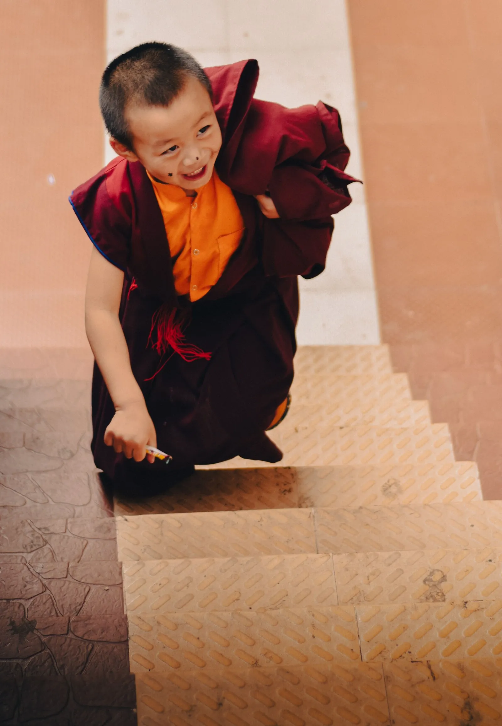 A young monk laughing as he climbs the steps of a temple in Gangtok