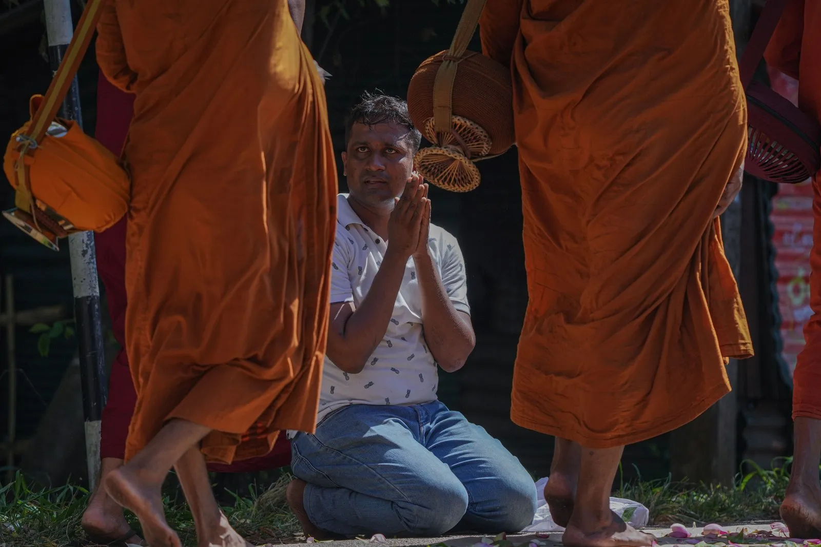 A man kneels in prayer as monks pass in procession, Anuradhapura