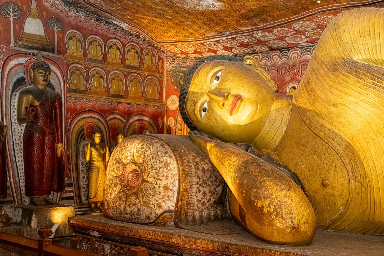 A reclining Buddha beneath the painted rock ceiling of a Dambulla cave temple