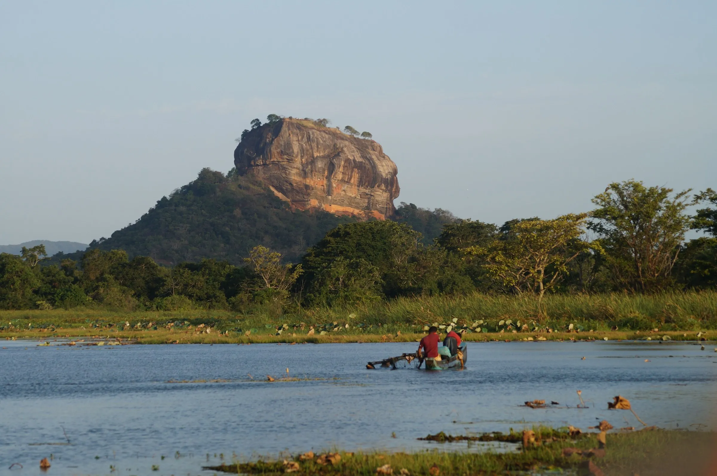Two fishermen in a boat on the water below the rock of Sigiriya