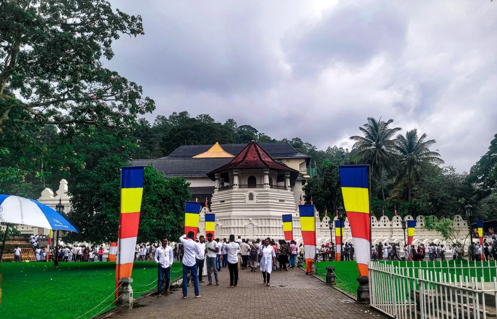 Pilgrims in white outside the Temple of the Tooth in Kandy, hung with Buddhist flags