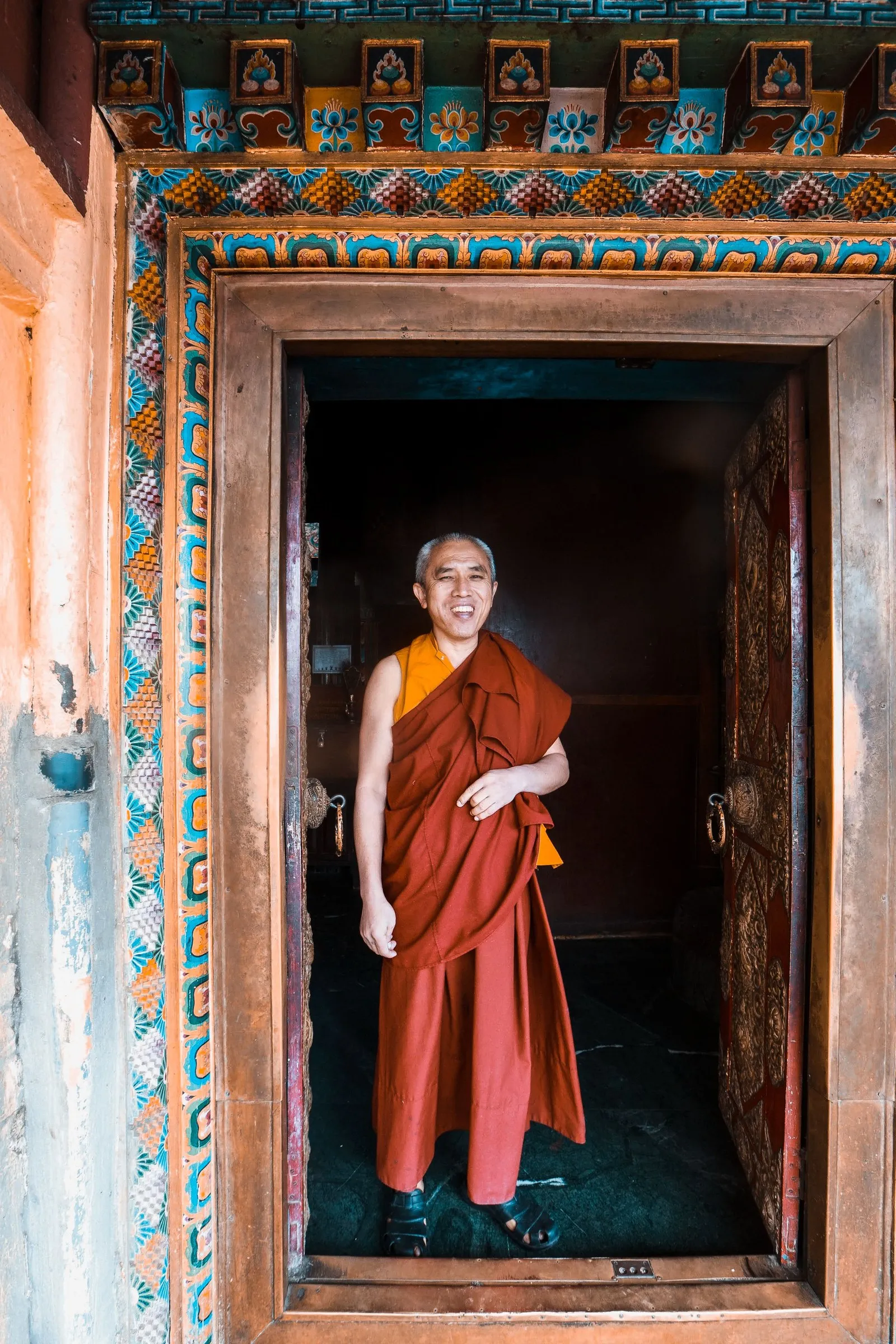 A monk smiling in the painted doorway of a temple, Bhutan