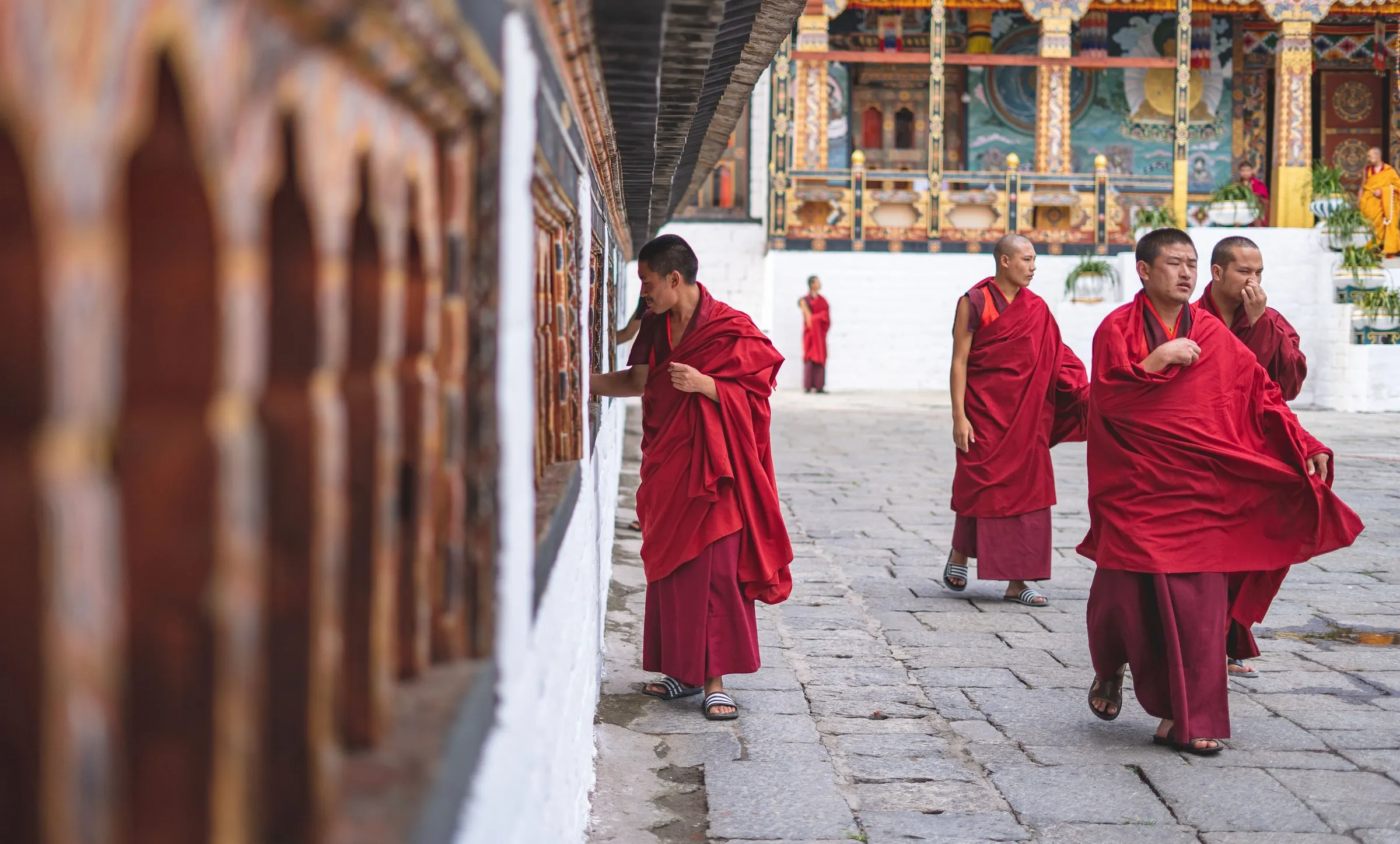 Monks walking past prayer wheels in a temple courtyard, Bhutan