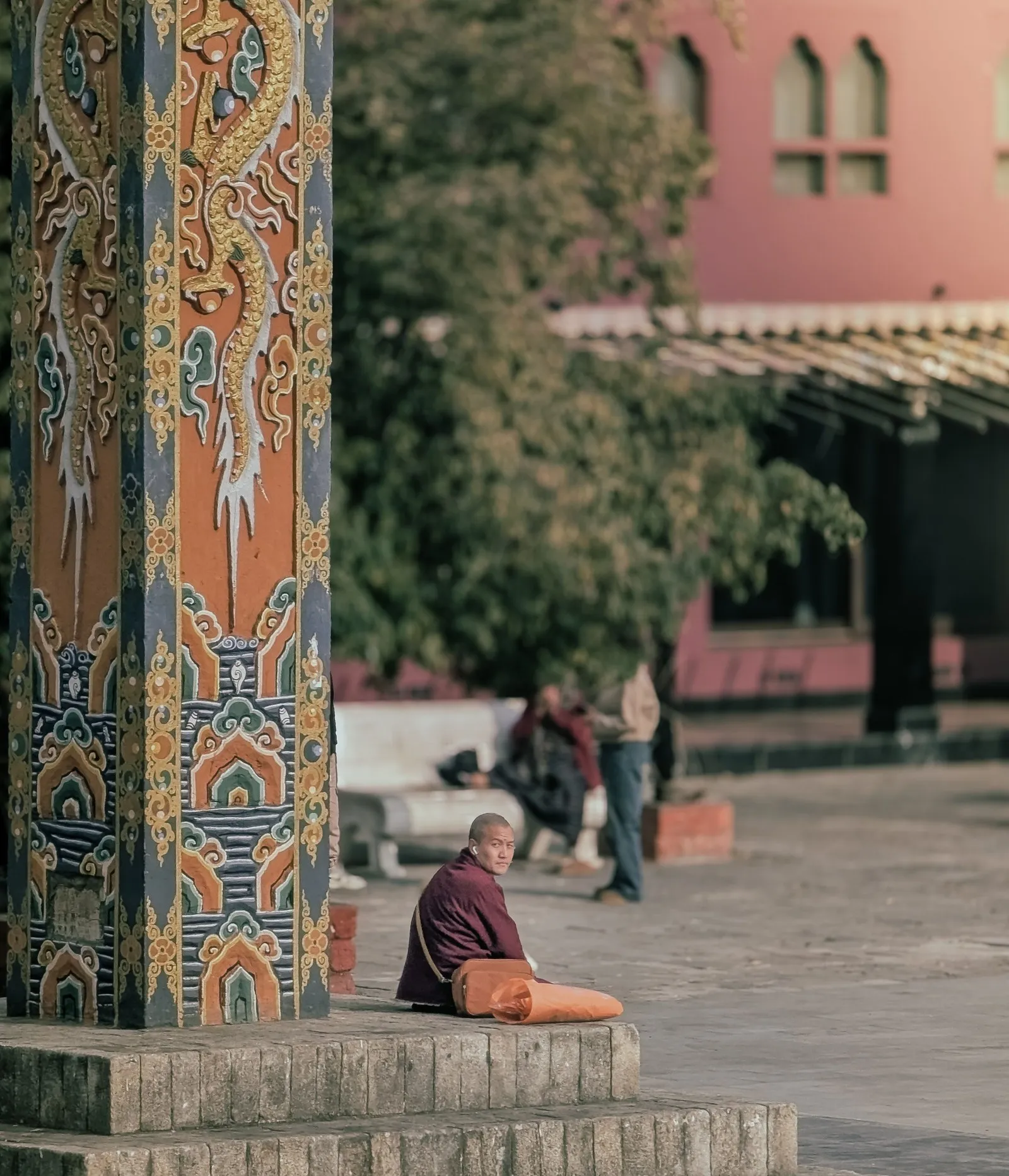 A monk sitting by a painted pillar in a temple courtyard, Bhutan