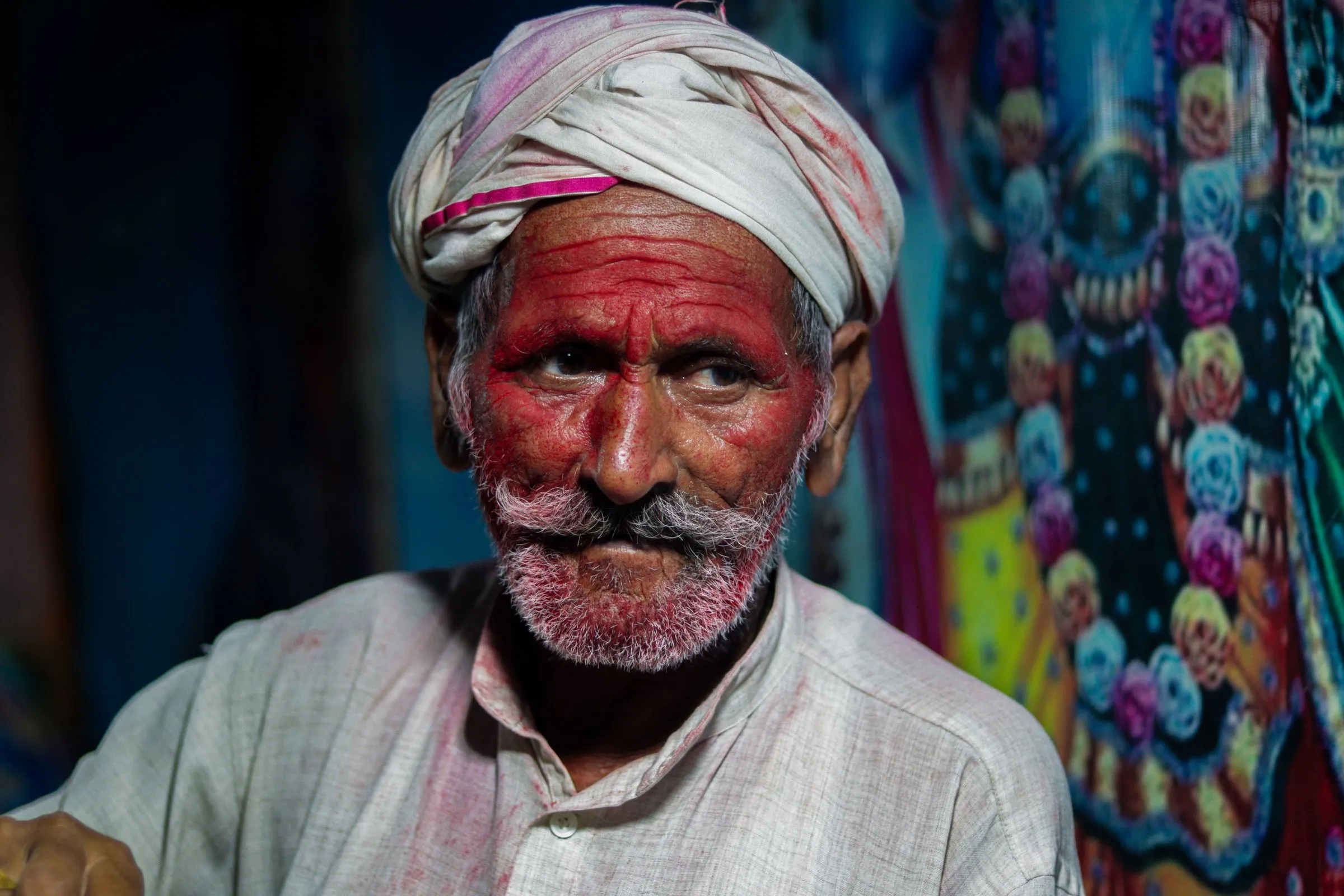 An elder in a white turban, his face red with gulal