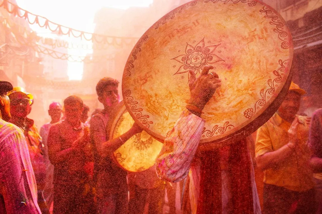 A man holding a wooden shield as colour flies at Nandgaon