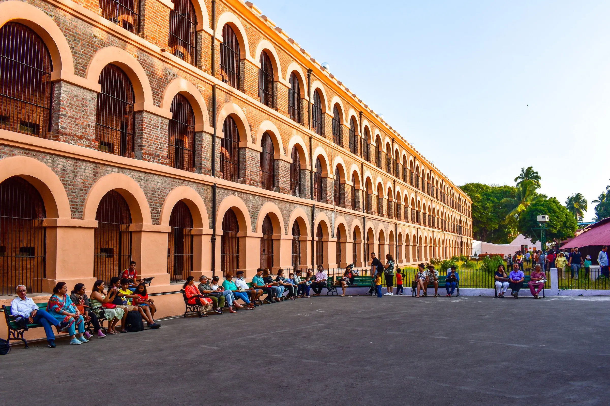 Visitors on benches below the arcaded brick wing of the Cellular Jail, Port Blair