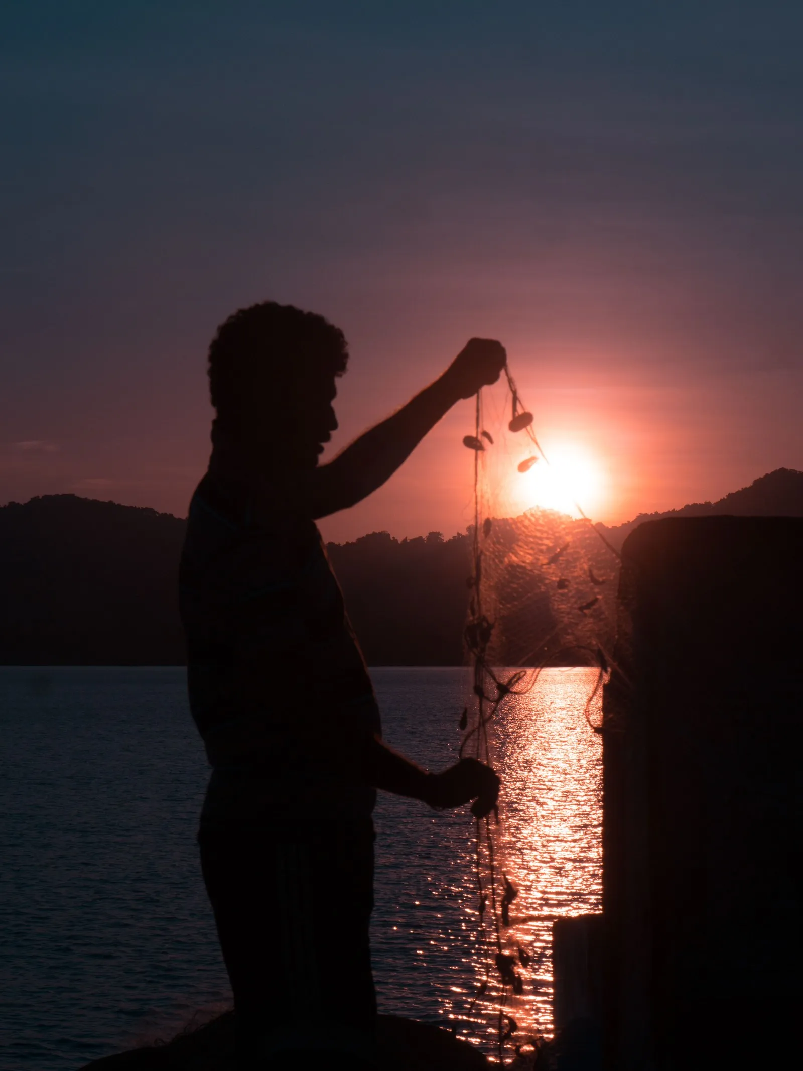 A fisherman sorting his net against the setting sun, Andaman Islands