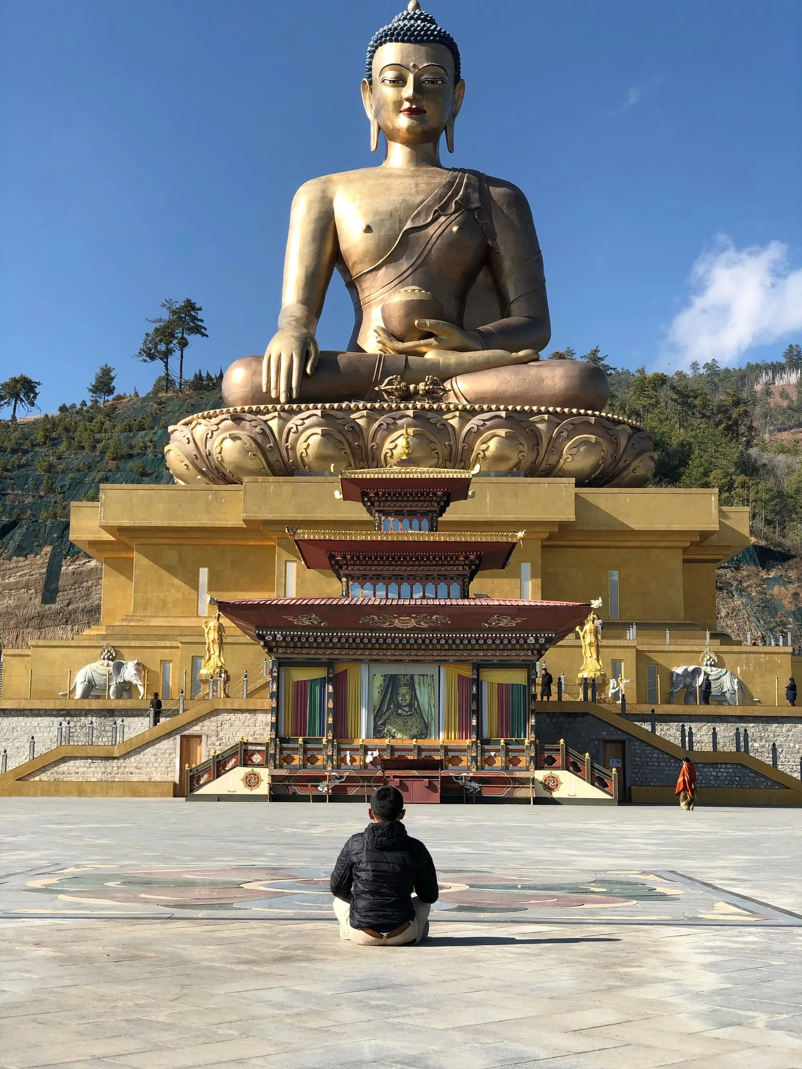A man seated in prayer before Buddha Dordenma above Thimphu