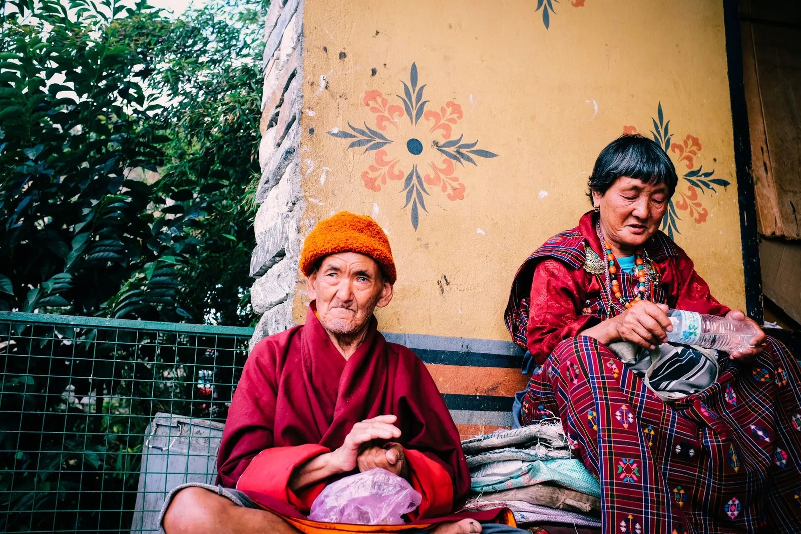 An elderly couple resting by a painted wall with their bundles of cloth, Bhutan