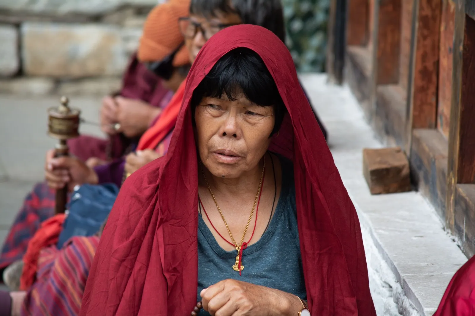 An elderly woman in a red shawl holding a hand prayer wheel, Thimphu