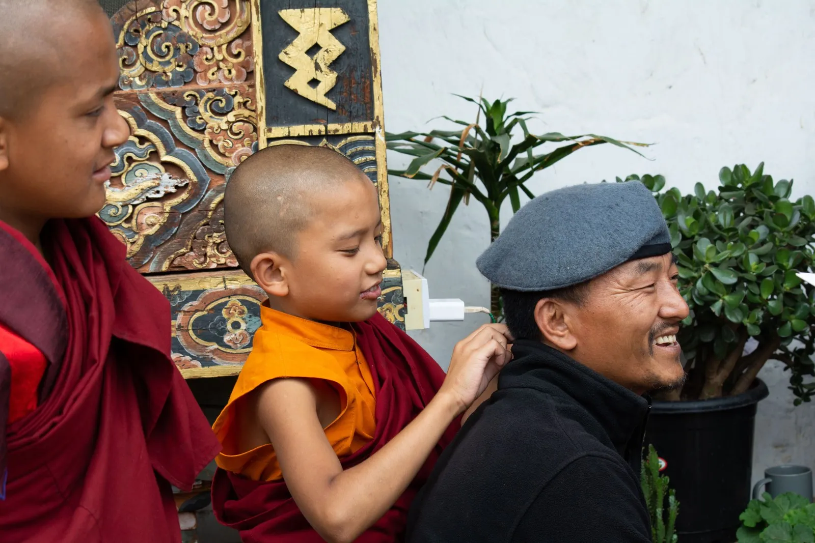 A young monk teasing a laughing man in a temple courtyard, Bhutan