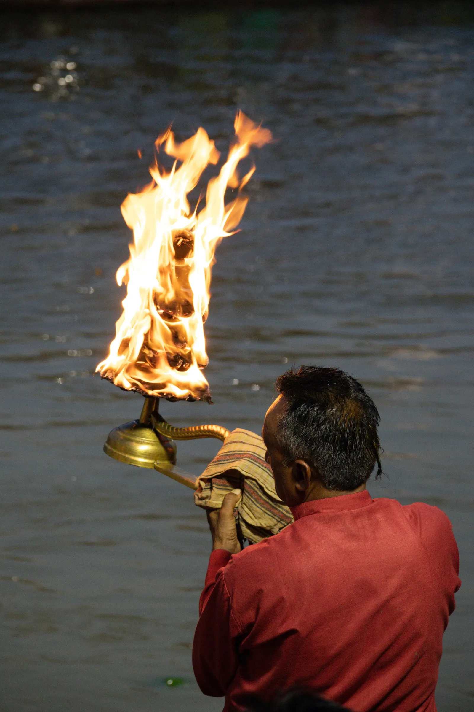 A man raising a fire lamp over the Ganga at the evening aarti, Haridwar