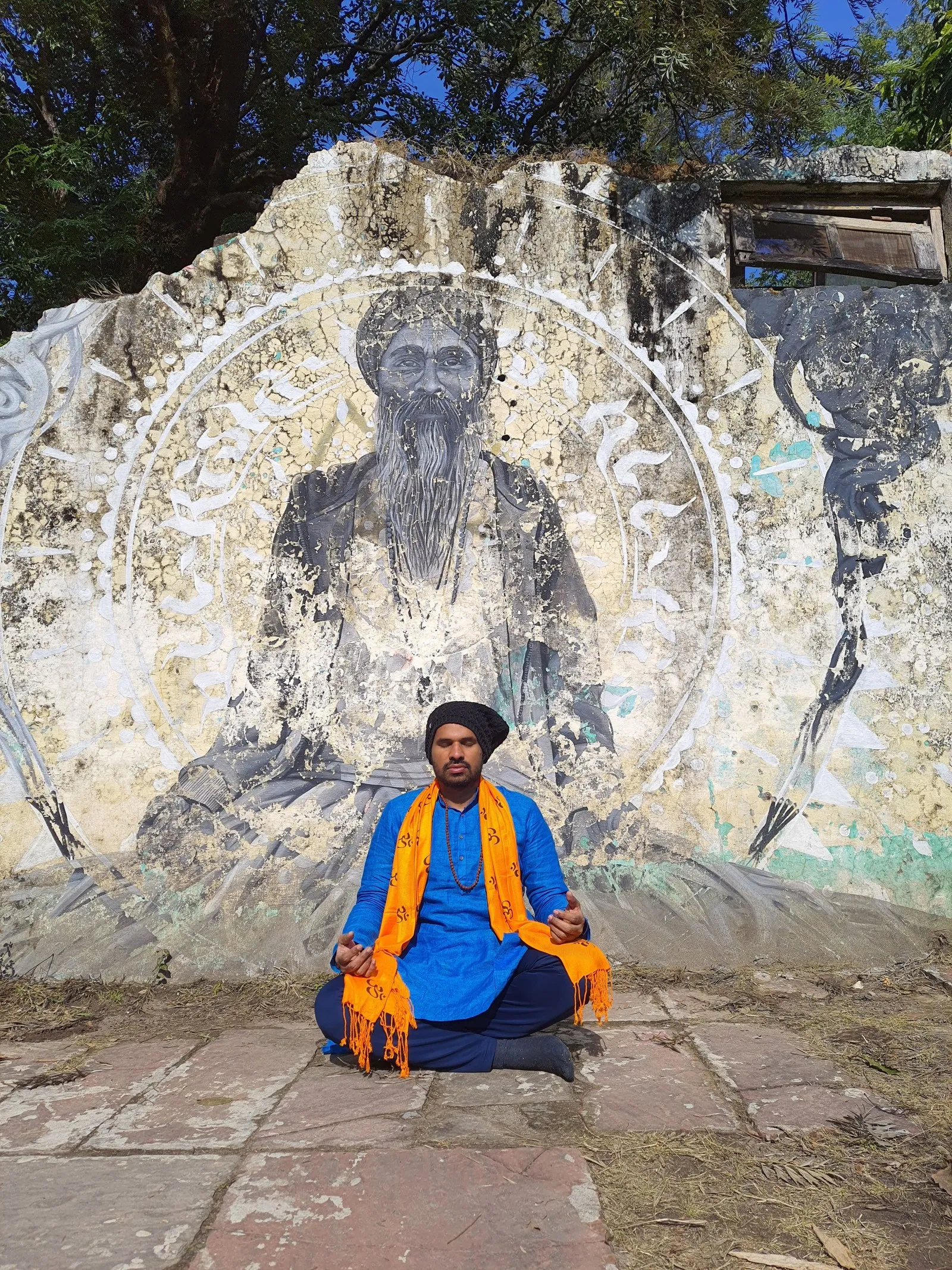 A man meditating in front of a painted mural, Rishikesh