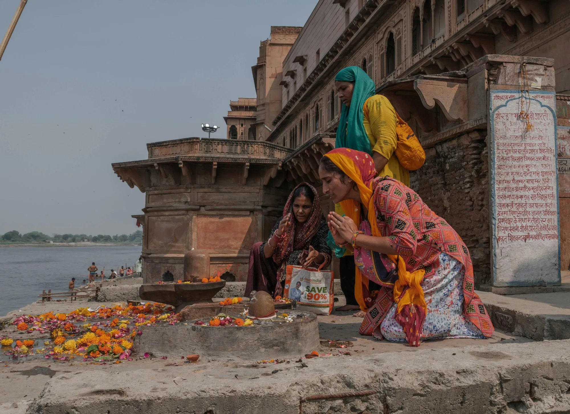 Women in bright saris praying with flowers on the ghat at Maheshwar