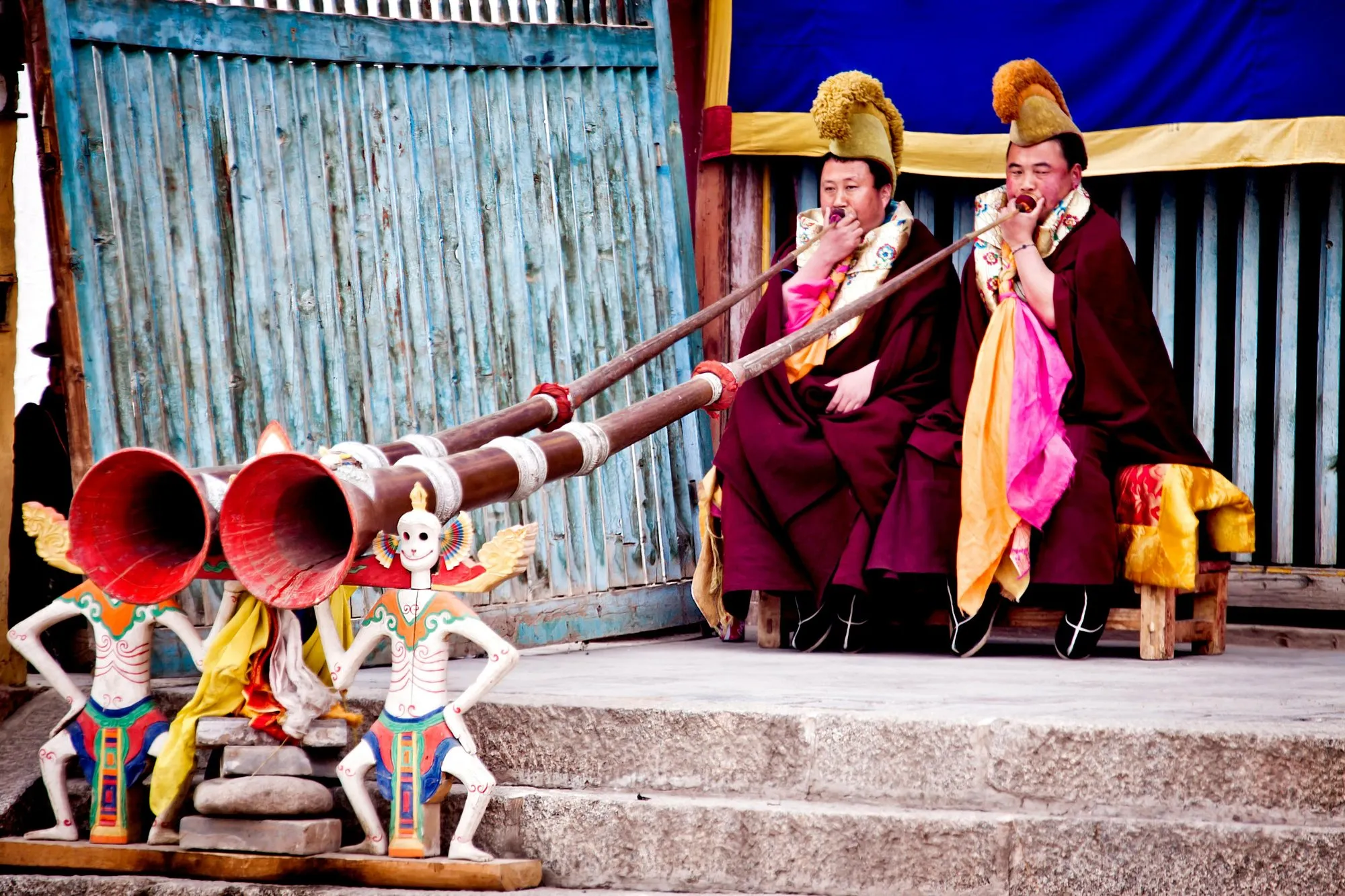 Monks sounding long horns beside painted guardian figures
