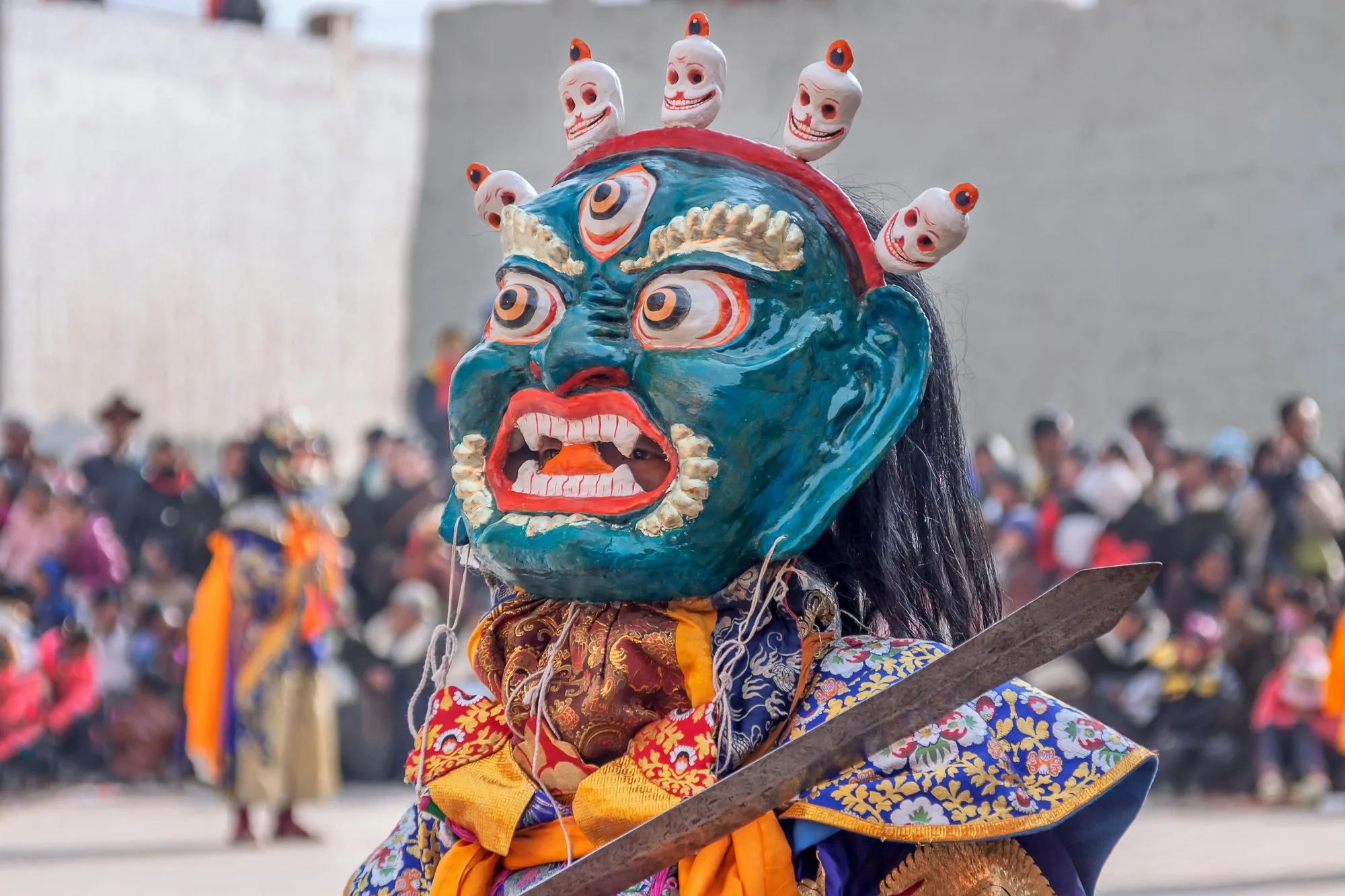 A Cham dancer in a blue wrathful mask crowned with skulls, holding a sword