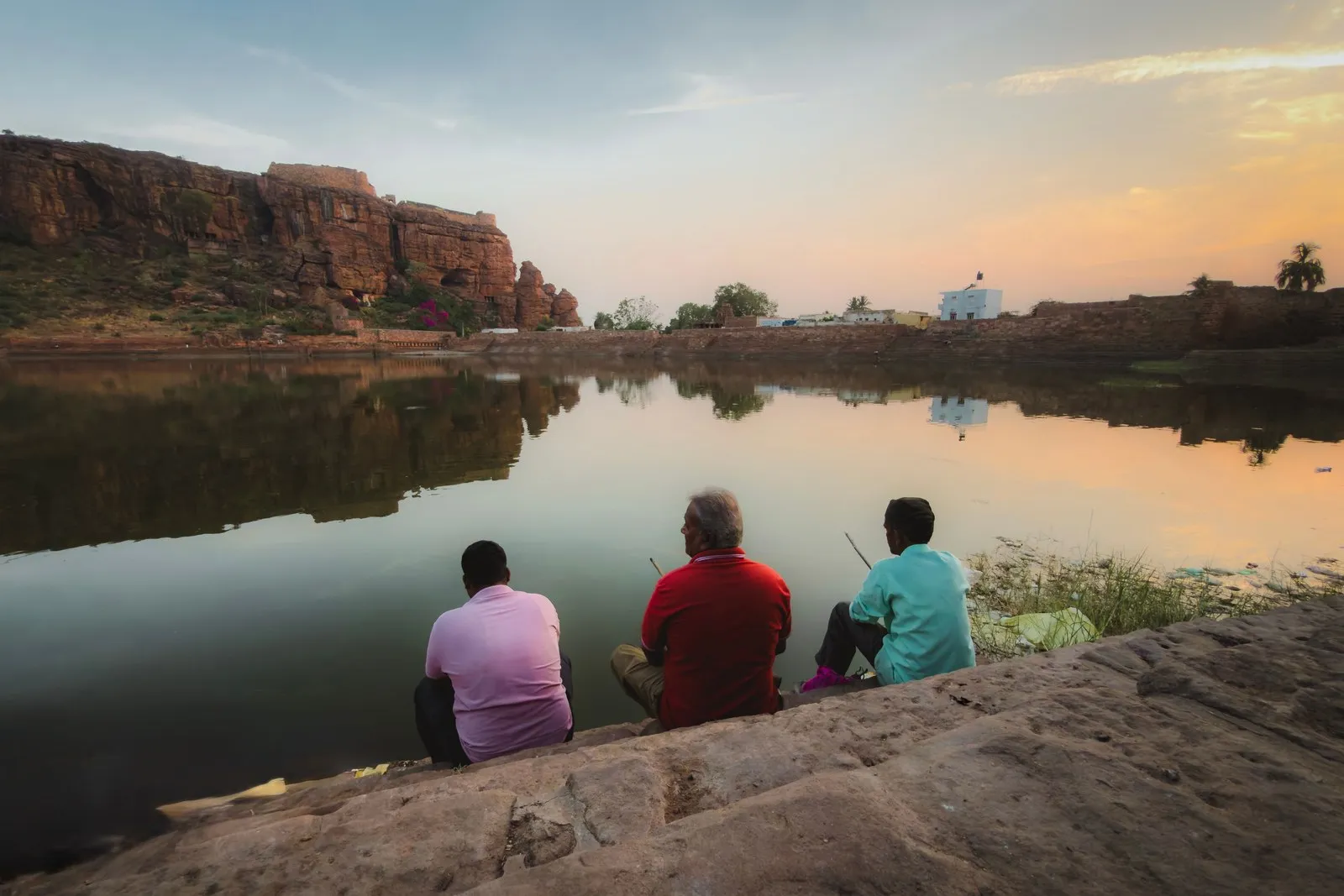 Three men fishing on Agastya Lake below the red cliffs of Badami at dusk