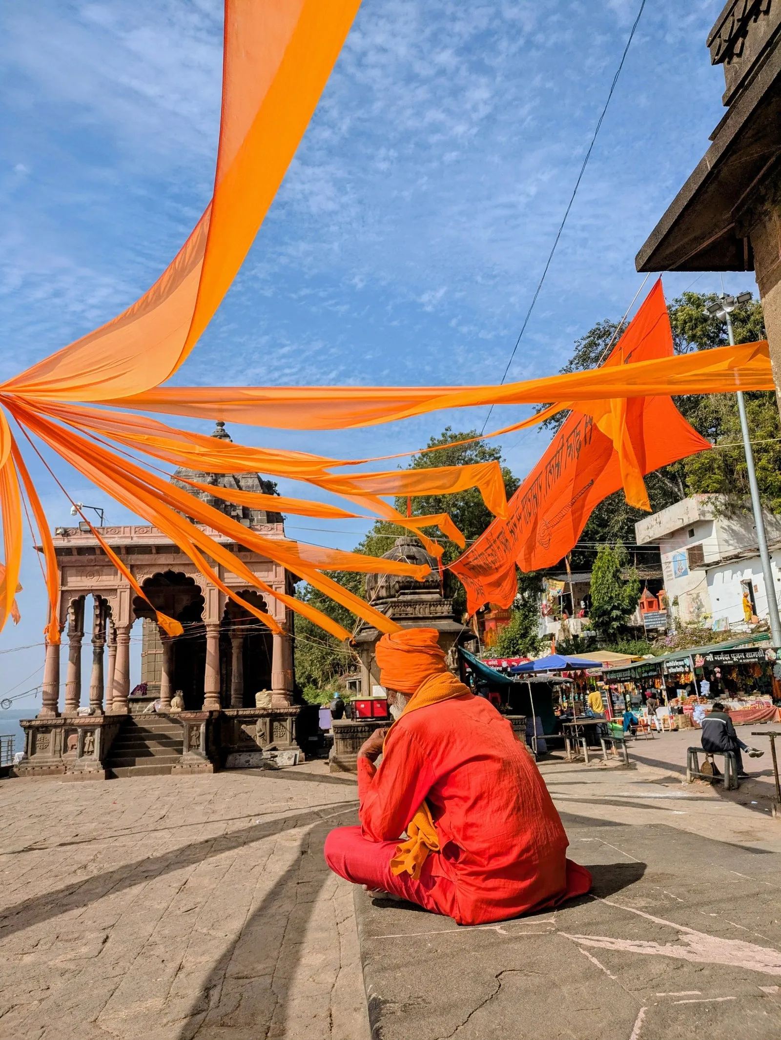A devotee in saffron on the ghats at Maheshwar, under temple flags