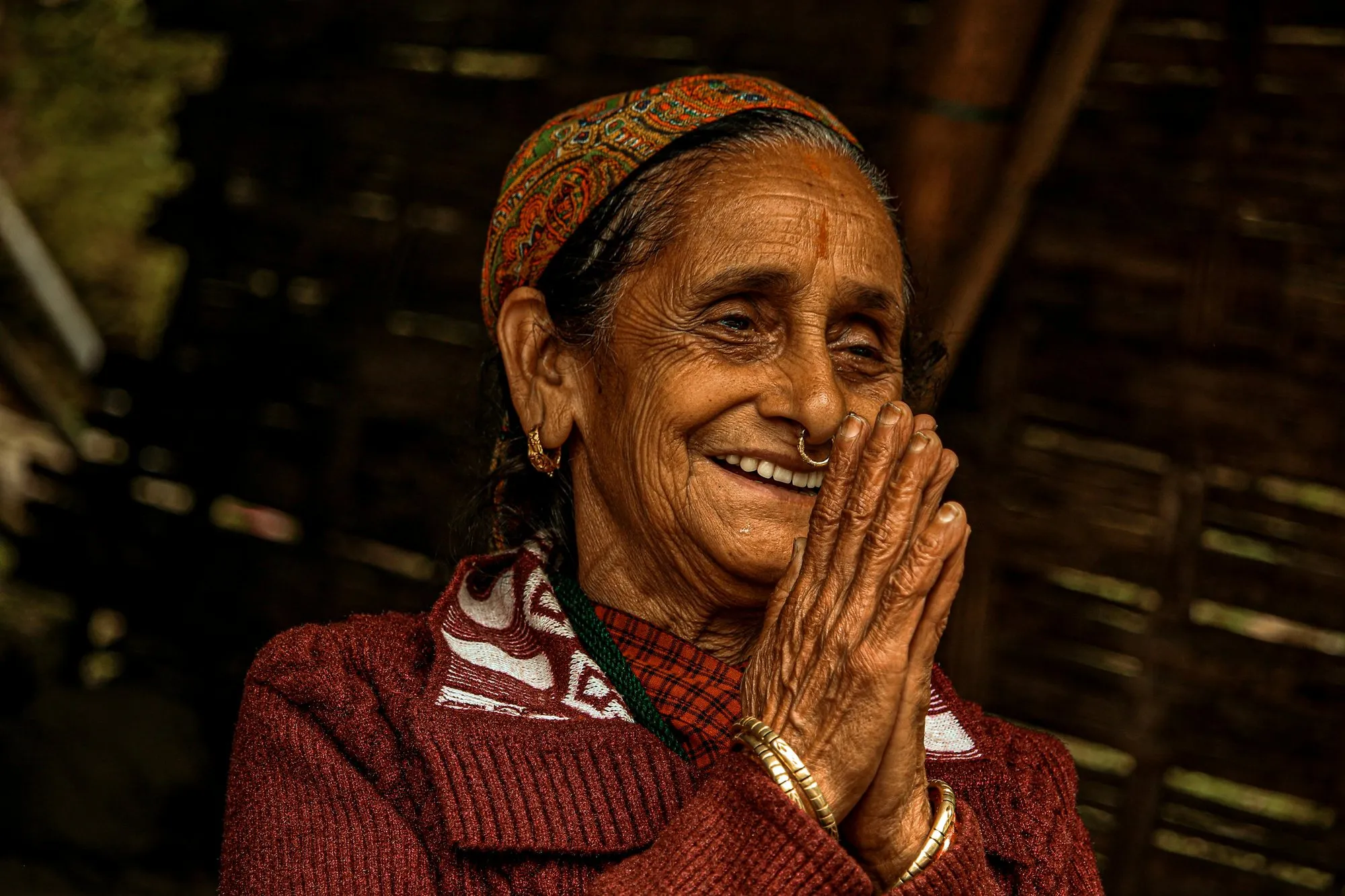 An elderly woman smiling, her palms joined in namaste