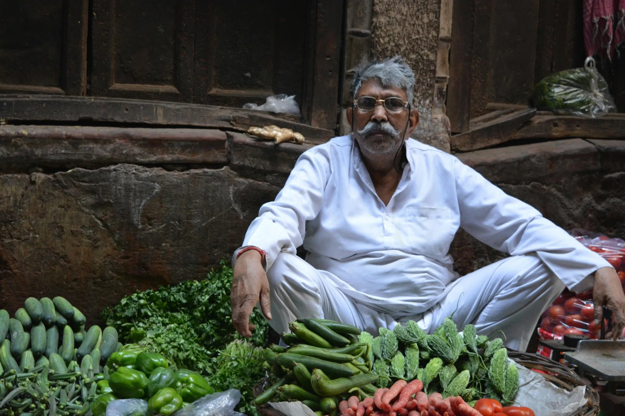 A vegetable seller in white seated among his produce