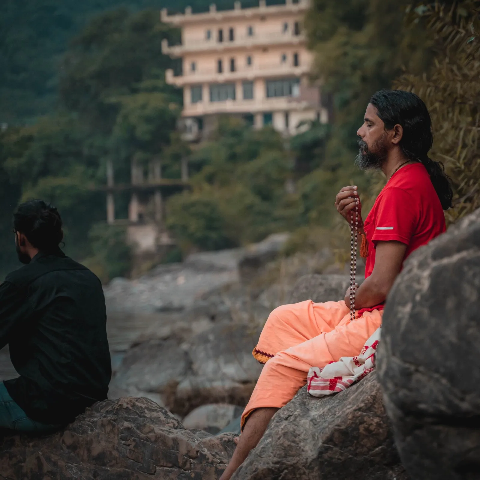 A man meditating with a mala on the rocks by the Ganga, Rishikesh
