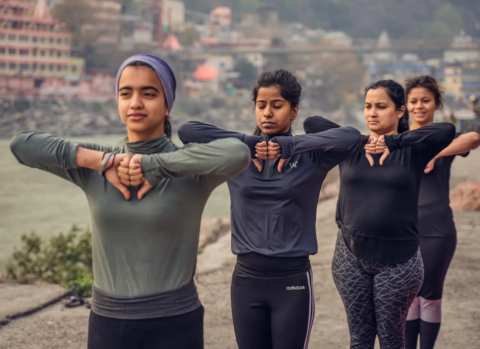 Four women warming up for yoga on the riverbank at Rishikesh