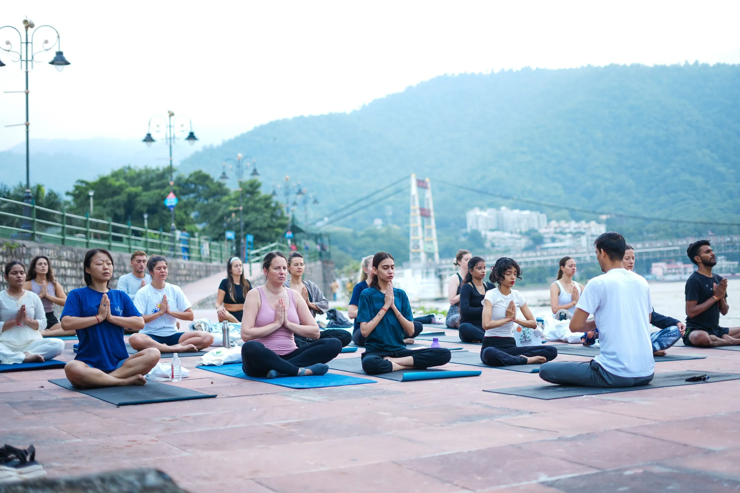 A yoga class on a riverside terrace at Rishikesh, a suspension bridge over the Ganga behind
