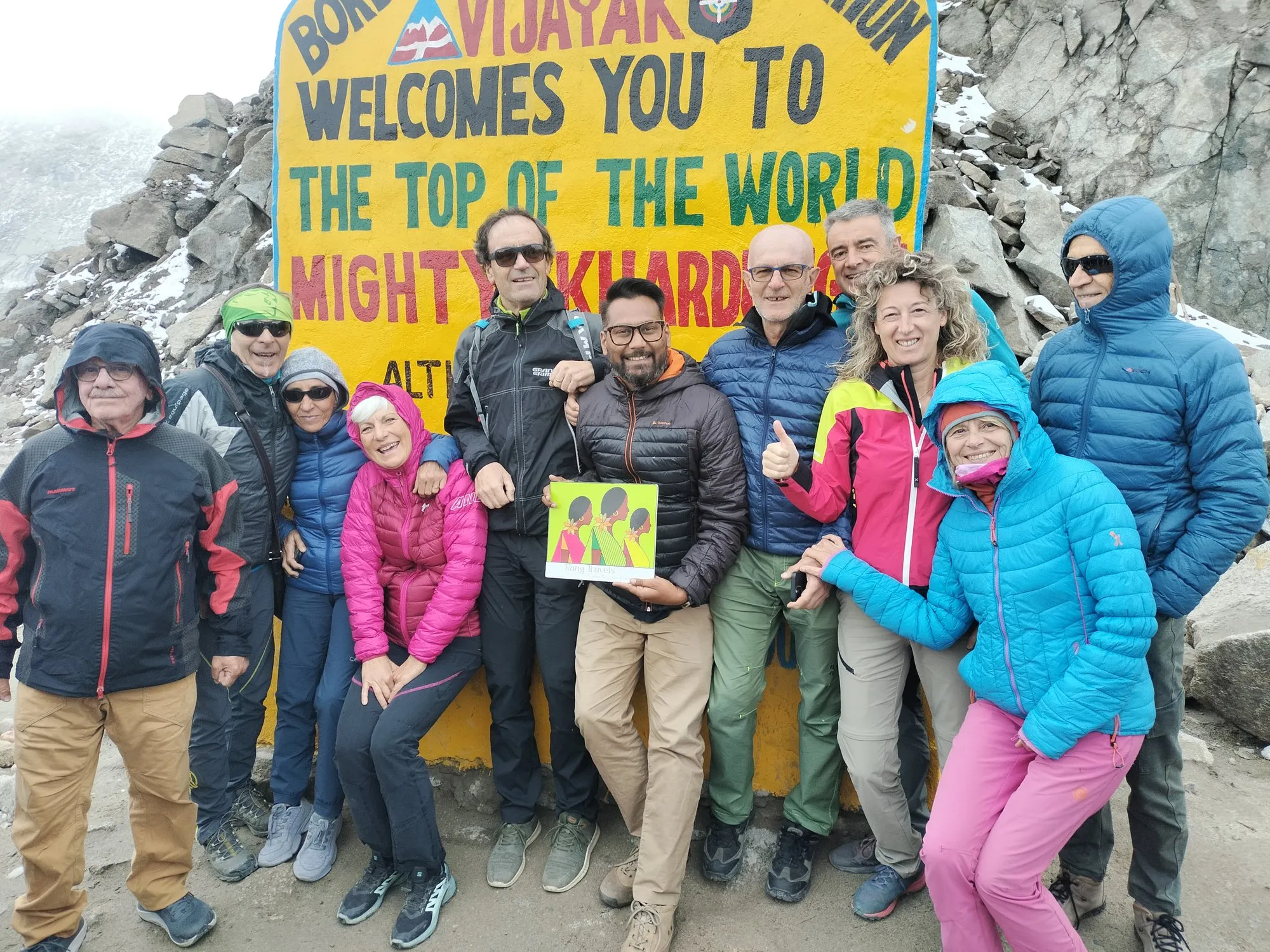 A group of travellers in down jackets at the sign on Khardung La