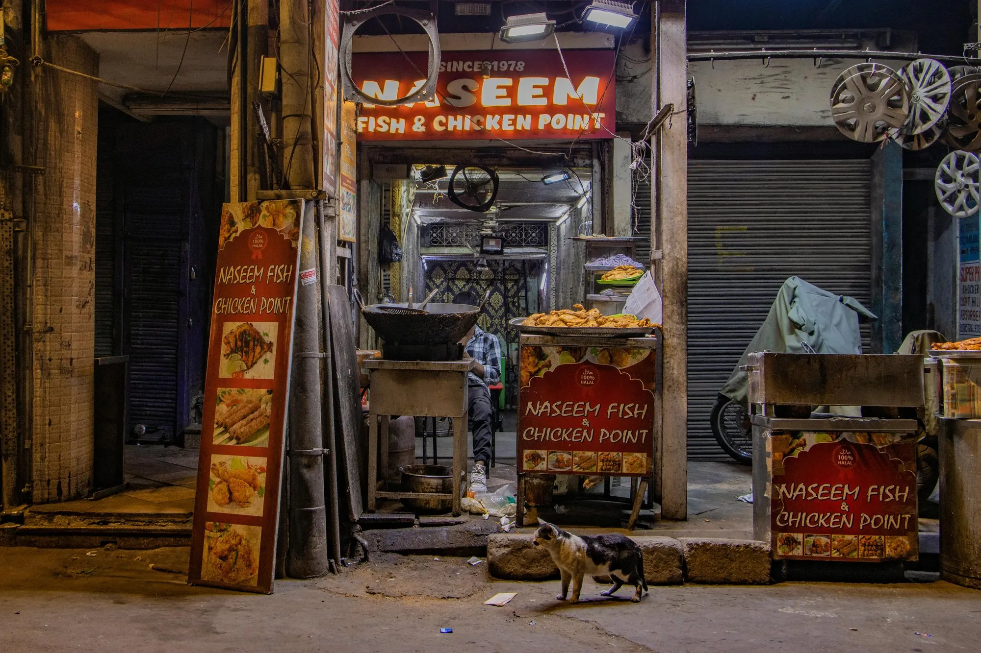 A lane of shuttered shops and a food stall at dusk