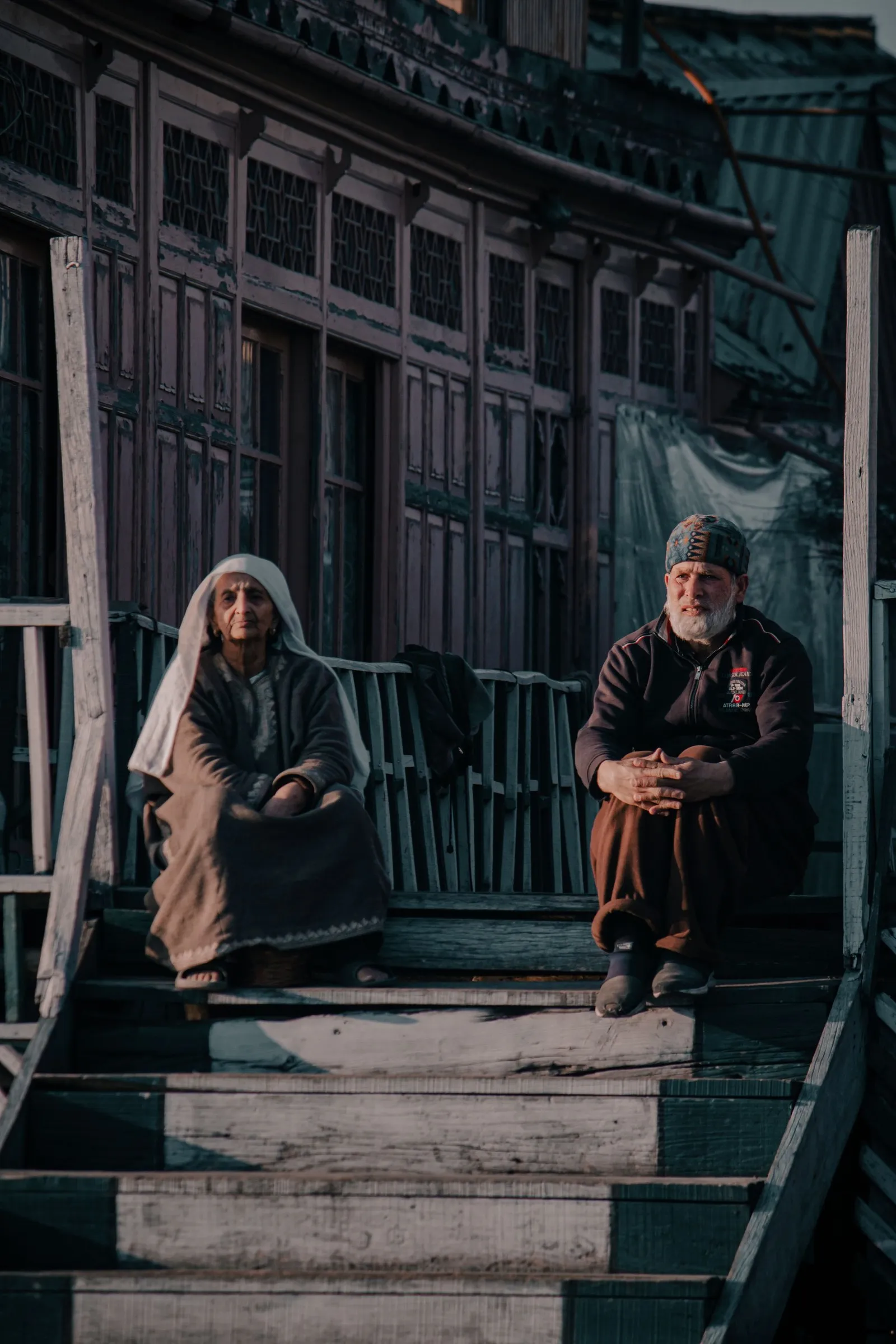 An elderly couple seated on the wooden steps of a houseboat, Srinagar