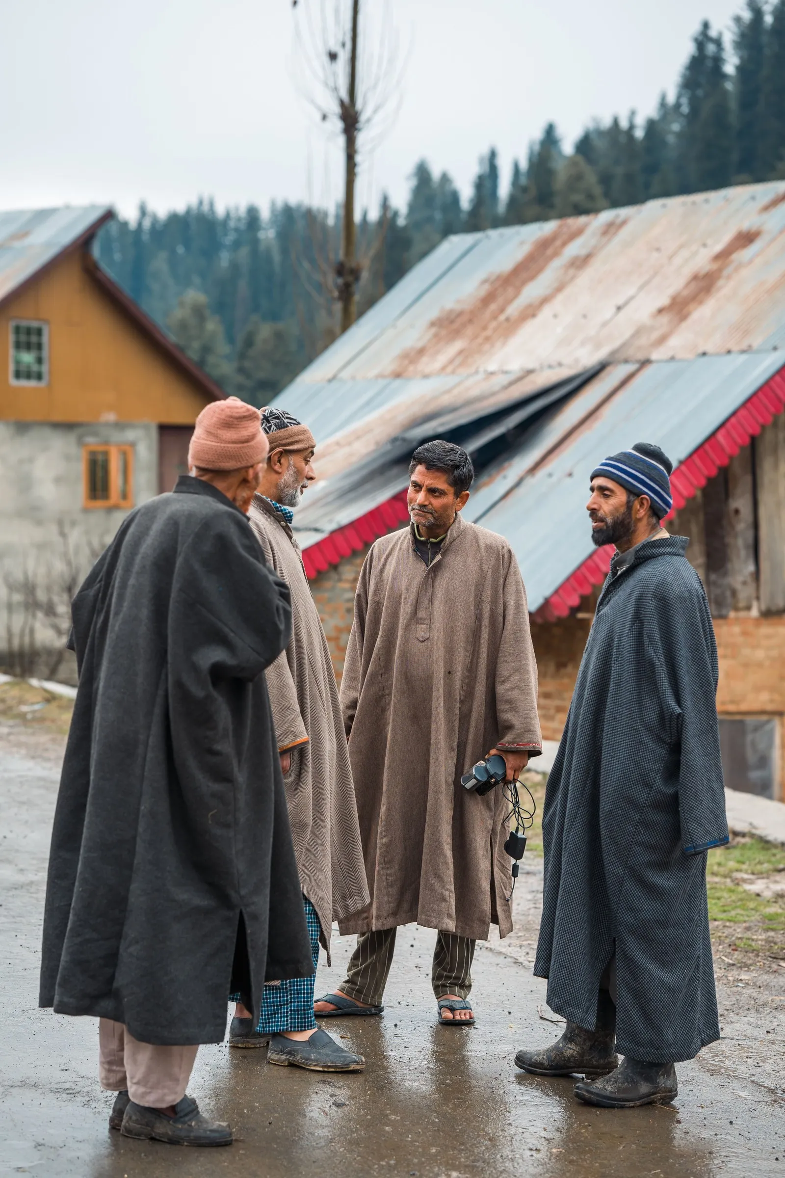 Men in woollen pherans talking on a village street, Kashmir