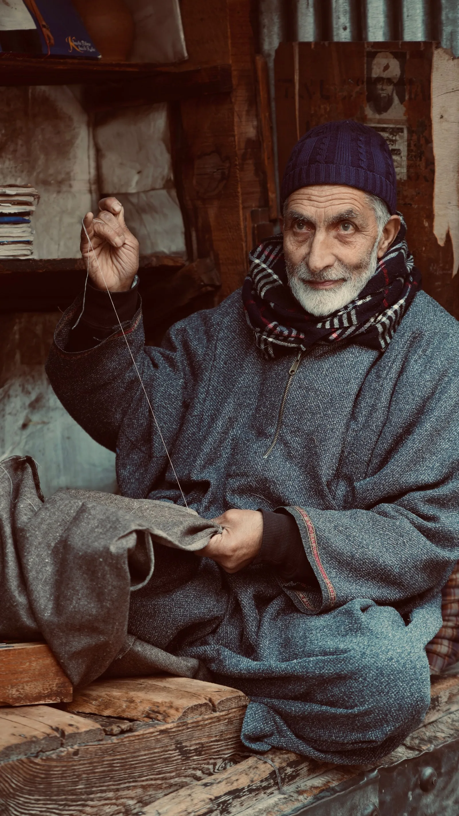 An elderly tailor in a pheran sewing by hand in his shop, Srinagar