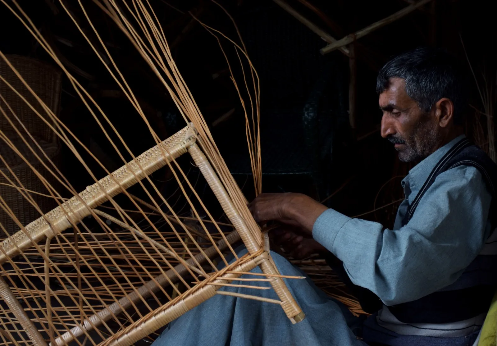 A craftsman weaving willow wicker by hand in his workshop, Srinagar