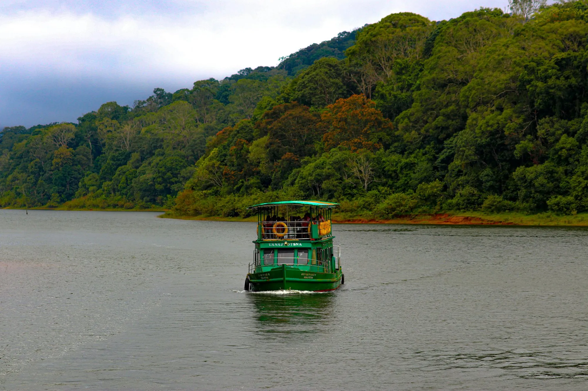 A green boat on Periyar Lake below forested hills