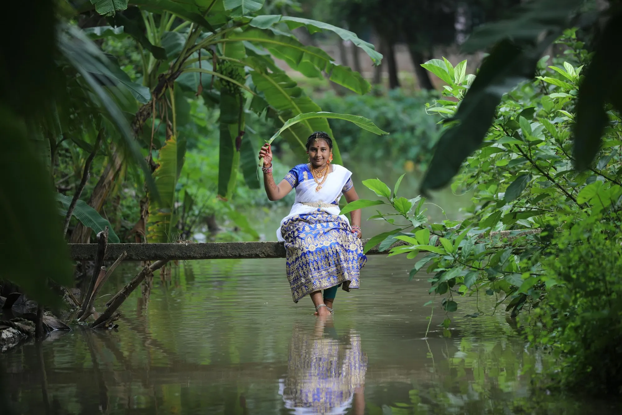 A woman in a white sari crossing a log over forest water